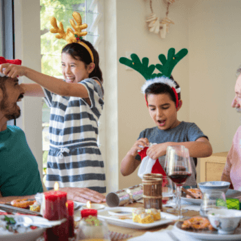 family at the table wearing reindeer earsindeer ears on. they are giving presents from under the christmas tree