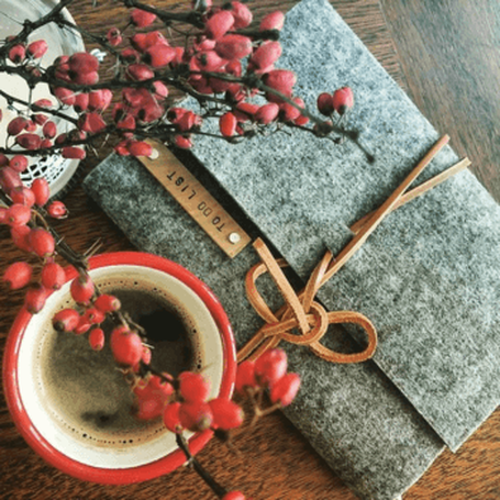 a red coffee cup with black coffee in it and a grey-green writing journal tide up with a leather string ready for writing down the one most important thing to make a Simply awesome Christmas