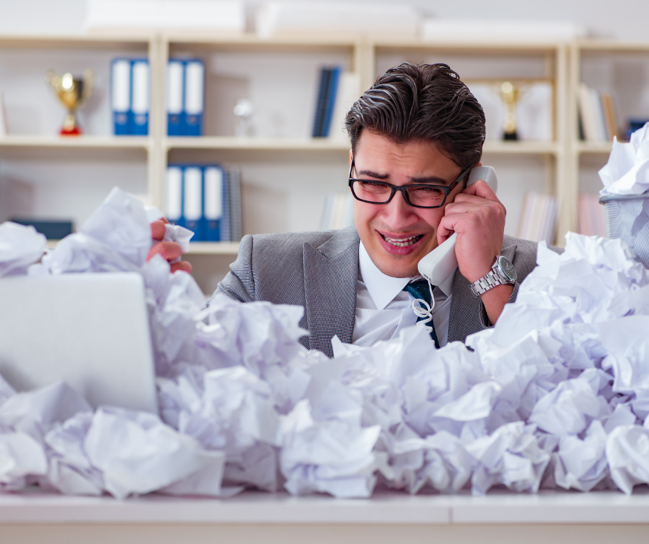 Man behind desk that is piled with scrunched up paper